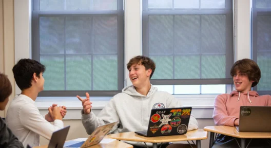 Three students at their desks having a conversation.