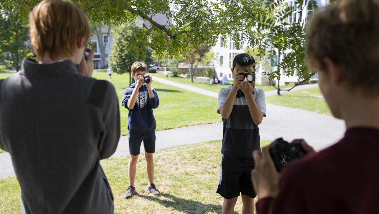 Four students face one another, each of them looking through a camera.