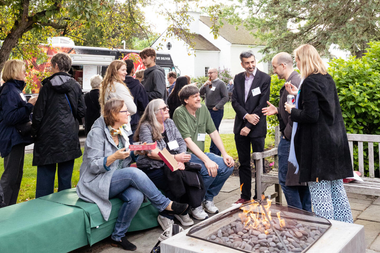 A group of people gather around a fire pit in a backyard