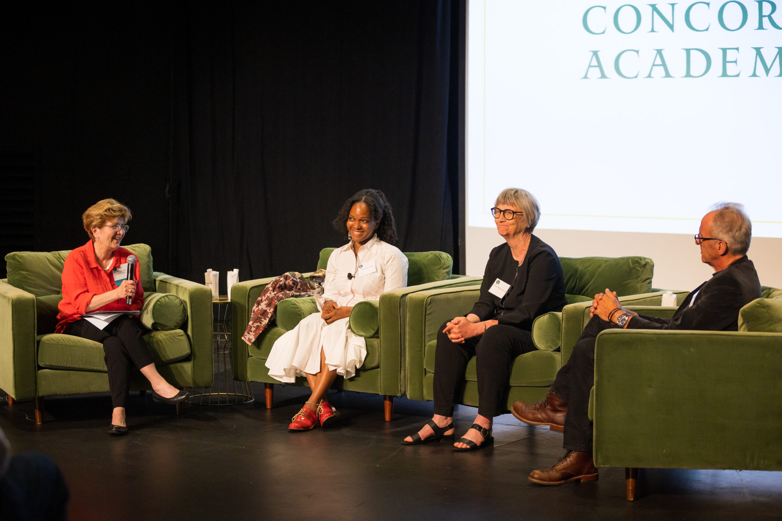 Four people sit on green velvet chairs facing the audience at a panel discussion