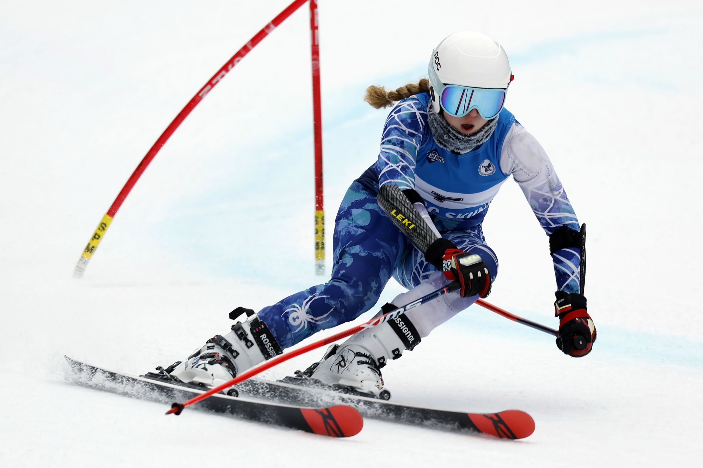 A female skier in a blue and white suit races down a snowy slope with her poles in hand