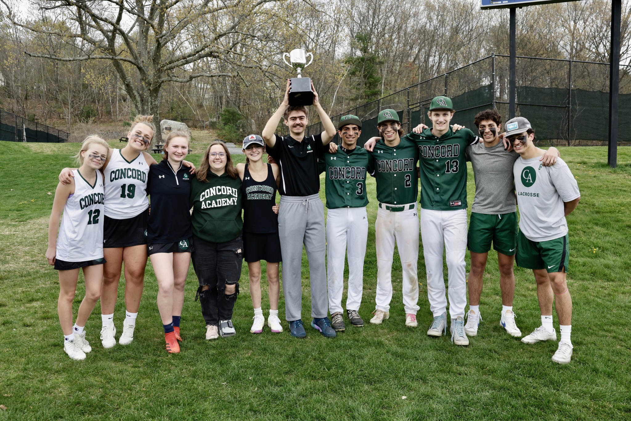 A group of students and their coach posing for a photo with their coach who is holding a trophy above his head