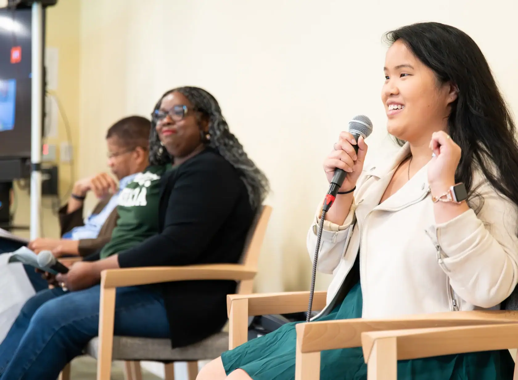 Three people sitting in a row, speaking in a conference room of people off screen - at the Alums and Students of Color Conference in 2024